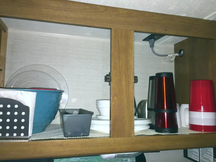 RV rental kitchen cabinet with stacking plates, bowls, cups, and a coffee maker. Outlet visible for appliances.. Keystone RV Summerland Mini 2015