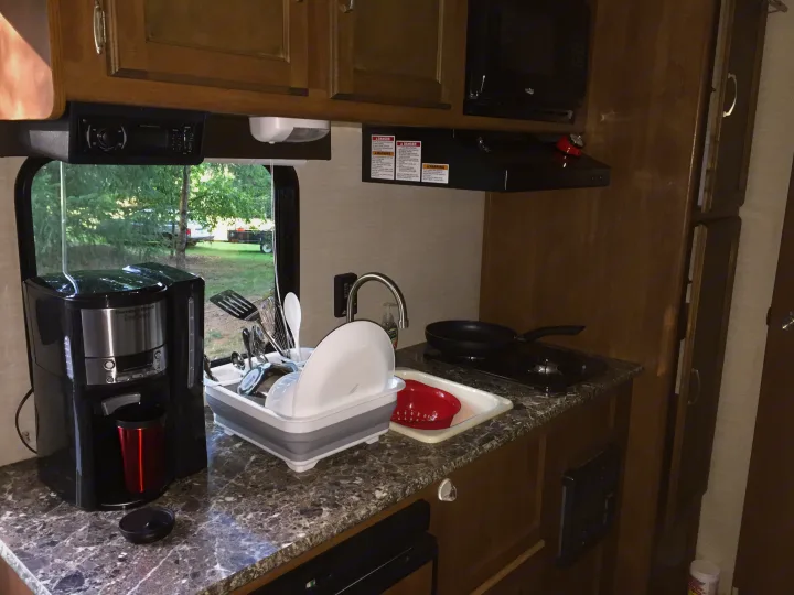 Inside an RV rental: a compact kitchen featuring a Hamilton Beach coffee maker, sink with dishes, stove, and microwave.. Keystone RV Summerland Mini 2015