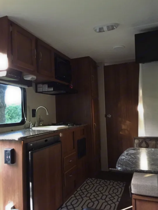 This RV rental interior features a kitchen with a microwave, sink, and wood cabinets, plus a dining/living area.. Keystone RV Summerland Mini 2015