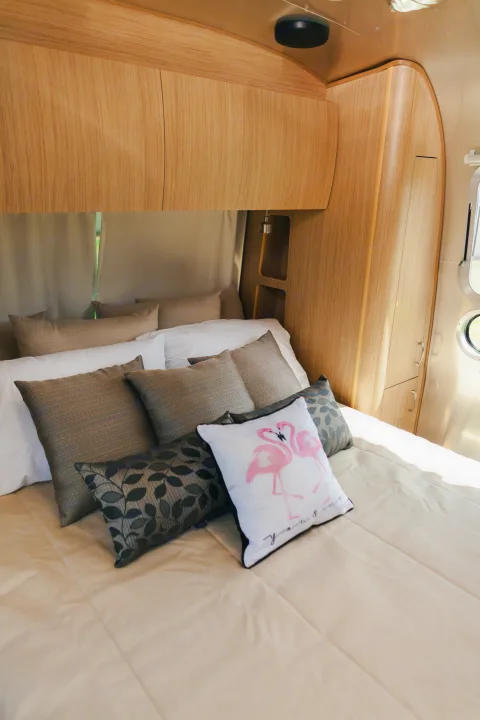 Cozy RV rental bedroom featuring a comfortable bed, light wood interior, and a fun flamingo pillow. Relax and travel.. Airstream Flying Cloud 2020