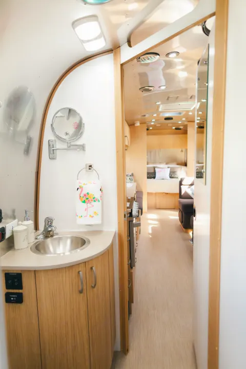 Bright, modern RV rental interior: Bathroom vanity with sink & mirror, leading to a comfortable living and bed area.. Airstream Flying Cloud 2020