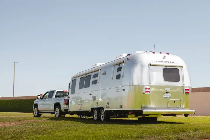 A silver Airstream RV rental, glistening in the sun, is hitched to a matching pickup truck on vibrant green grass under a clear blue sky.. Airstream Flying Cloud 2020