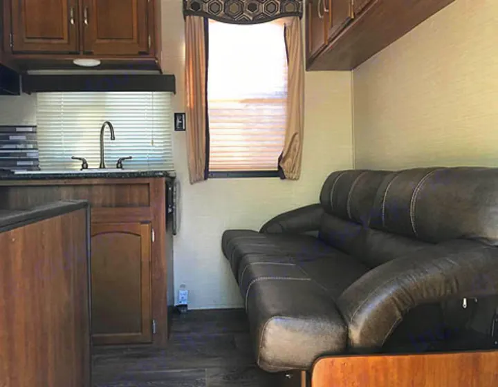 An inviting RV rental interior: kitchen with sink & wooden cabinets, opposite a comfortable sofa.. Keystone Springdale 2017