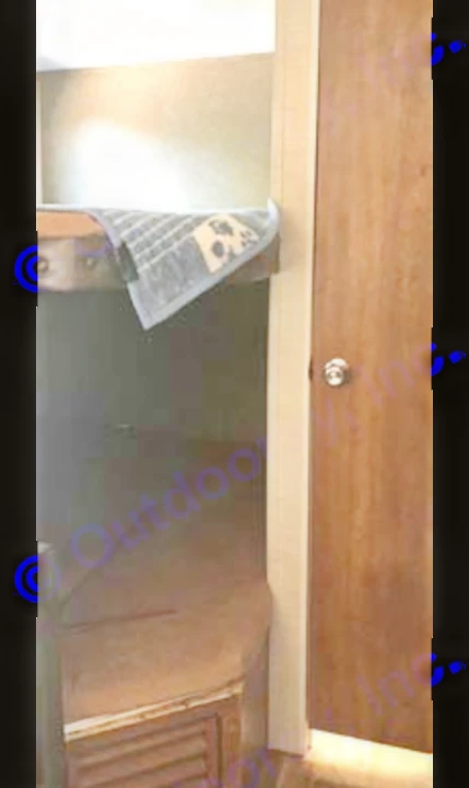 Compact RV rental interior showing a bunk bed with a patterned towel, a lower mattress, and a wooden door.. Keystone Springdale 2017