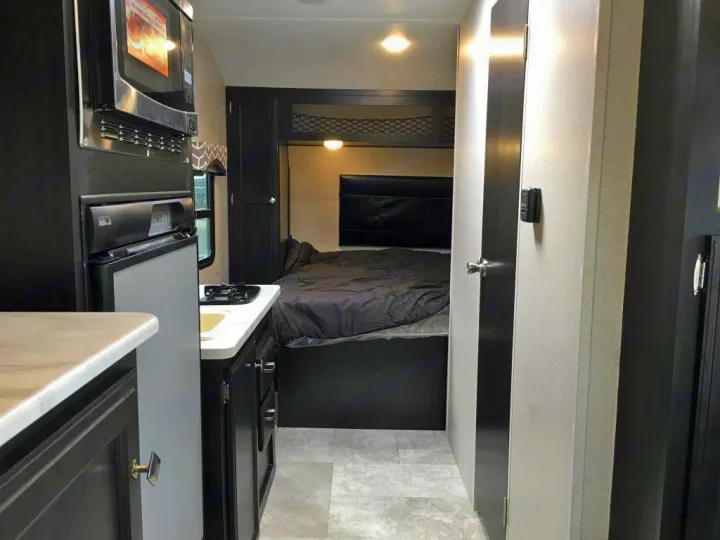 RV rental interior shows a compact kitchen with microwave, fridge, and stovetop, leading to a cozy bedroom area.. Venture Rv Sonic Lite SL 169VRD 2018