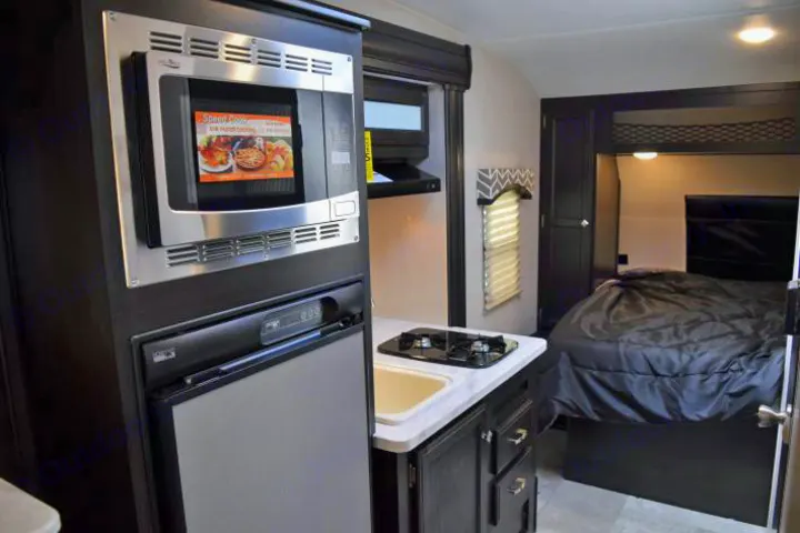 RV rental interior showcasing a compact kitchen with microwave, fridge, stove, and a comfortable sleeping area with a bed.. Venture Rv Sonic Lite SL 169VRD 2018