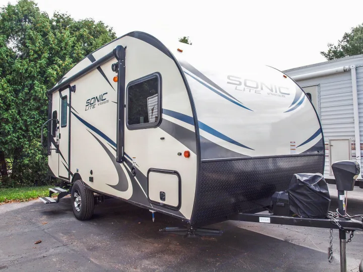 Sleek Sonic Lite travel trailer RV rental, light-colored with blue accents, parked on asphalt.. Venture Rv Sonic Lite SL 169VRD 2018