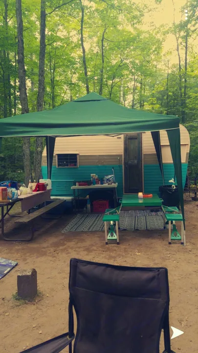 Cozy campsite with a retro RV rental under a green canopy amidst lush trees, perfect for outdoor adventures.. Nomad Rear fold 1962