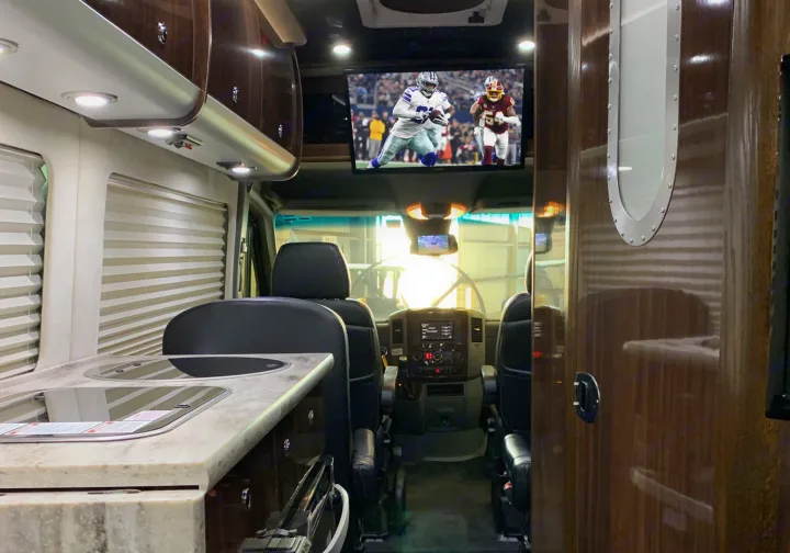 Spacious, luxurious rv rental interior with TV playing football, kitchenette, and cockpit. Ideal for premium travel entertainment.. Airstream Interstate 2015