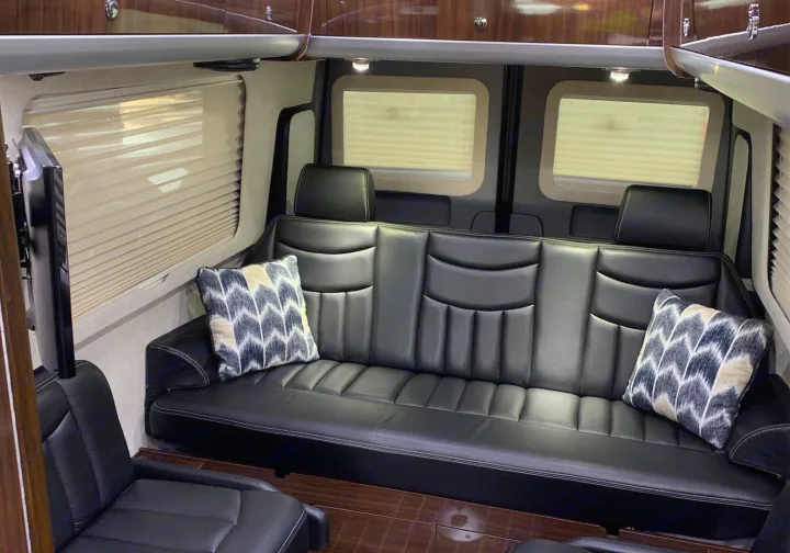 RV rental interior featuring a plush black leather sofa, two separate seats, privacy blinds, and wood flooring for luxury travel.. Airstream Interstate 2015