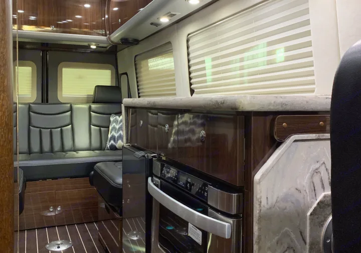 Spacious RV rental interior with a cozy seating area, kitchen counter, built-in oven, and elegant wood cabinetry.. Airstream Interstate 2015