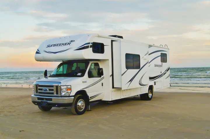 White Sunseeker RV rental parked on a sandy beach at sunset, with ocean waves and birds in the background.. Other Other 2019