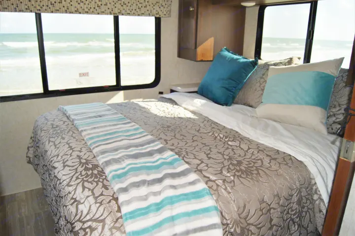 RV rental bedroom with stunning ocean views. A cozy bed with teal & grey pillows and striped blanket, overlooking beach waves.. Other Other 2019