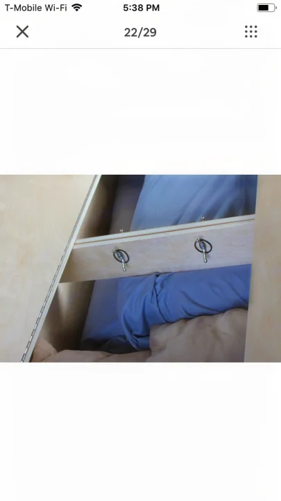 RV rental: Detailed view of a custom-built wooden bed platform with secure pins, hinges, and bedding inside.. ram promaster city 2016