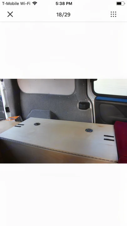 Inside this RV rental, see a light wood bed platform with hardware, upholstered walls, and a red cushion for comfort.. ram promaster city 2016