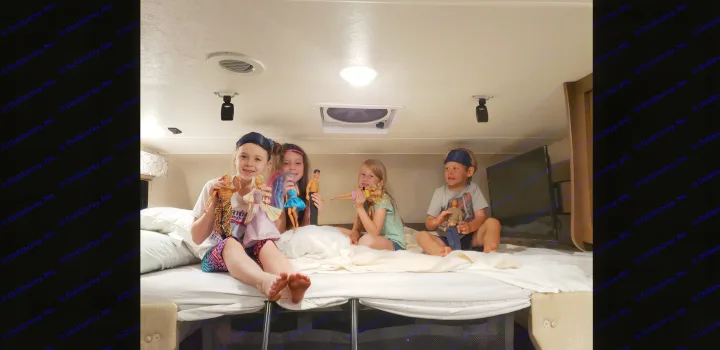 Four children play with dolls on a bed inside an RV rental, enjoying their travels. Happy family fun on the road.. Coachmen Freelander BH31 2019