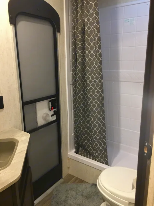 Compact RV rental bathroom showing shower, toilet, vanity, and a unique internal screen door.. Starcraft Autumn Ridge 2018