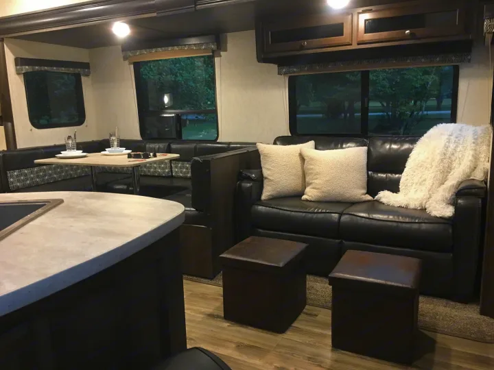This cozy RV rental interior features a dining booth, black leather sofa with white pillows, and overhead cabinets, offering a comfortable living space.. Starcraft Autumn Ridge 2018