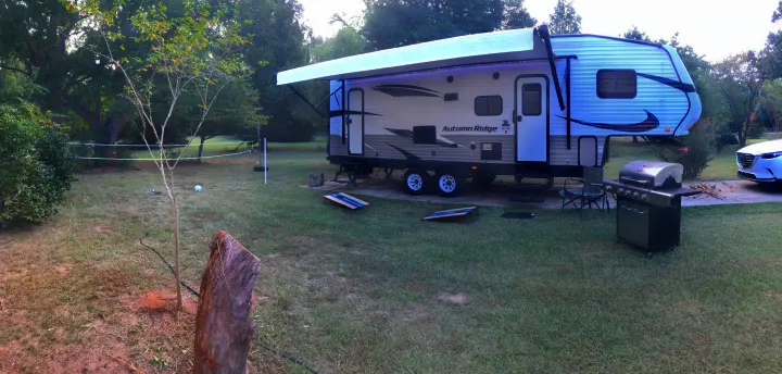 Spacious RV rental setup in a serene backyard, complete with awning, grill, cornhole, and volleyball net for outdoor fun.. Starcraft Autumn Ridge 2018