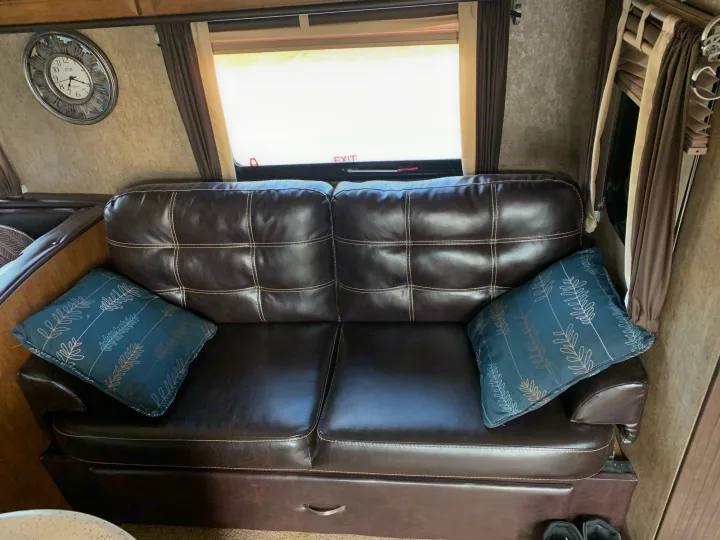 Inside an RV rental: a brown leather sofa with decorative pillows, a window, and a wall clock in the living area.. Forest River Wildwood 2017