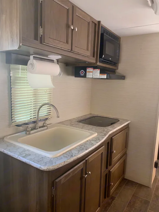 Kitchen area featuring large farm-style sink, 2 burner cook top and microwave. Keystone Bullet 2018