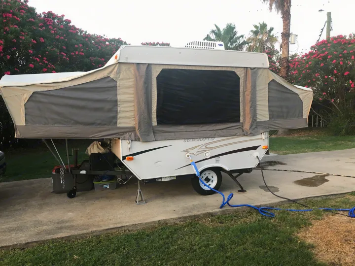 Pop-up RV rental ready for adventure. Shows the camper extended with water and electric hookups at a paved campsite.. Starcraft St 2006