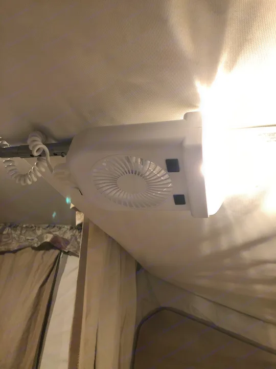 A white ceiling fan and light combo unit with a coiled power cord, mounted inside an RV rental, illuminating the fabric interior.. Starcraft St 2006