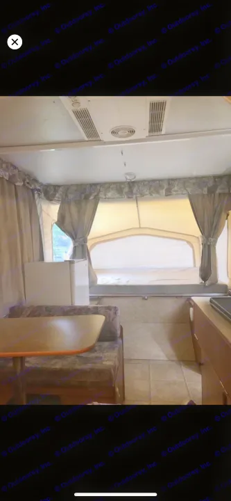 Interior of a pop-up RV rental, showing a bed, dinette with table & benches, and a small fridge.. Starcraft St 2006