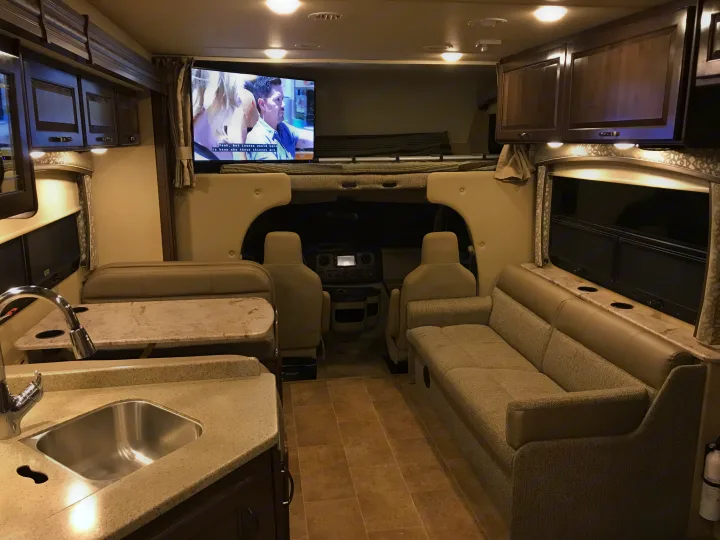 Spacious rv rental interior showing full kitchen, dining booth, living sofa, overhead bunk bed, and front cockpit area.. Thor Chateau 2020