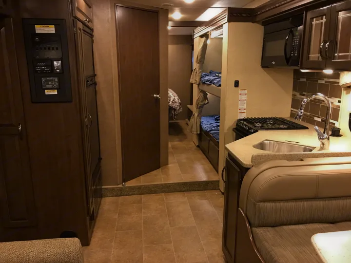 Inside an RV rental: view from dinette, showing kitchen, microwave, bunk beds, and main control panel.. Thor Chateau 2020