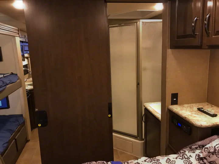 Compact bathroom with shower, sink vanity, and adjacent bunk beds visible in this RV rental interior.. Thor Chateau 2020