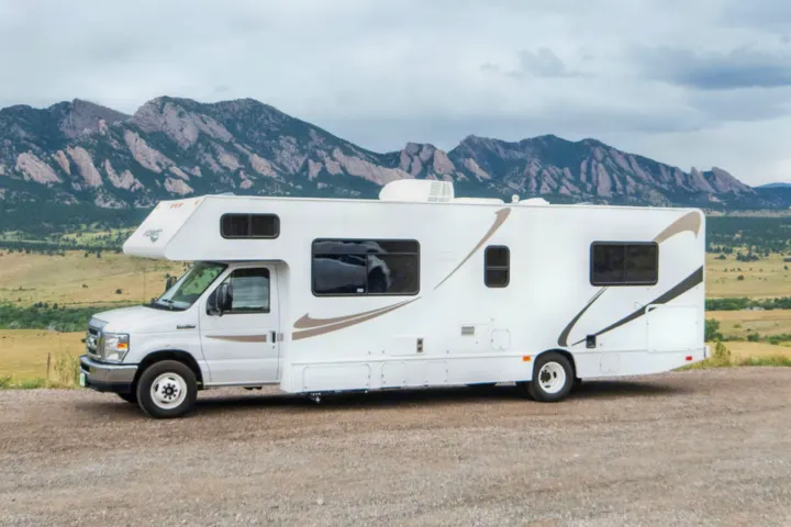 White RV rental parked on a gravel road with scenic mountains and fields in the background under a cloudy sky.. Other Other 2015