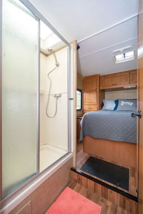 Explore this RV rental's interior: a bright, compact shower and a cozy, elevated bedroom with warm wood cabinetry.. Other Other 2015
