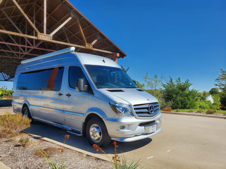 Silver Airstream RV rental, a Mercedes-Benz Sprinter van, under a timber pavilion on a sunny day.. Airstream Interstate 2015