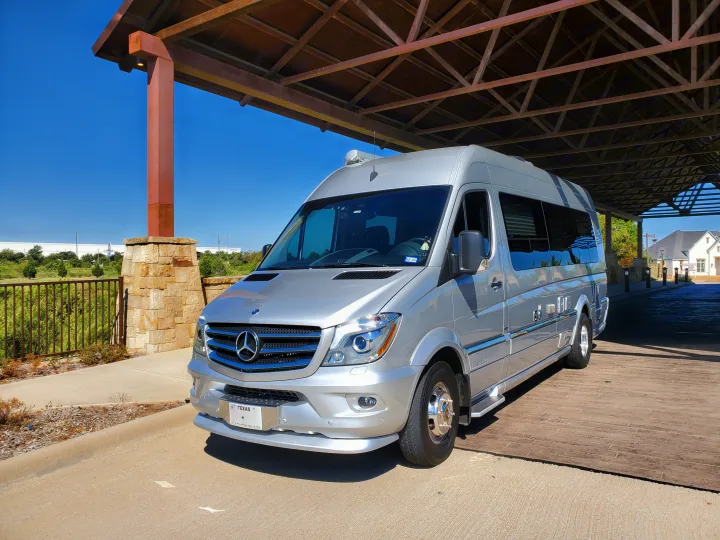 Silver Mercedes-Benz Sprinter RV rental parked under a large brown canopy on a sunny Texas day.. Airstream Interstate 2015