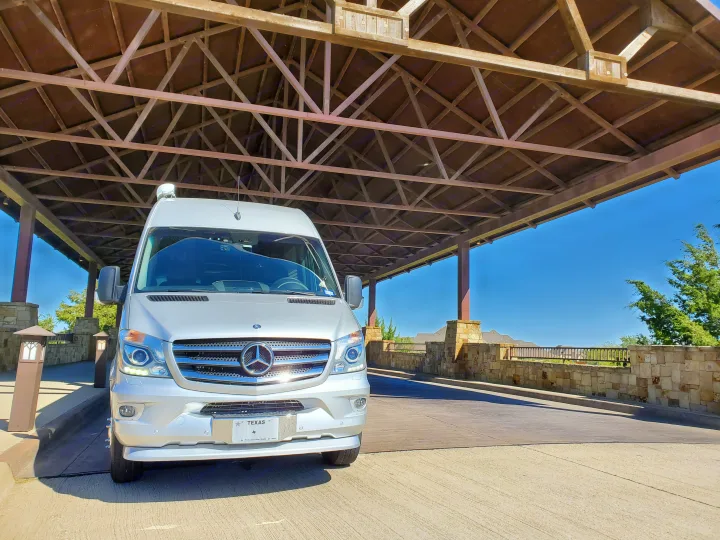 A sleek silver Mercedes Sprinter van, ready for your next rv rental adventure, parked under a beautiful wooden porte-cochère.. Airstream Interstate 2015