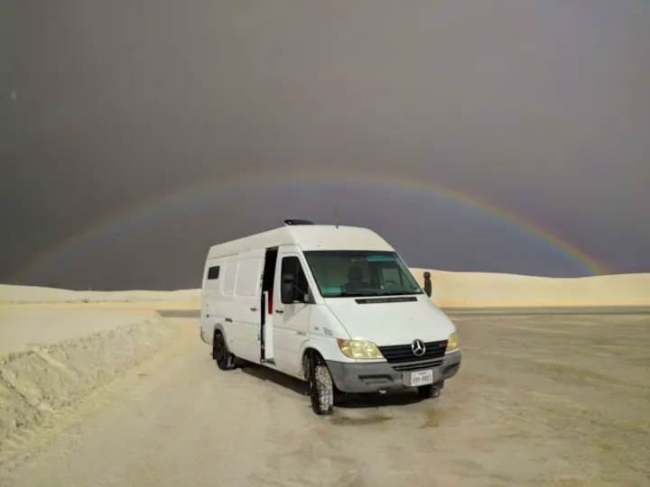RV rental camper van parked on White Sands' gypsum with a rare rainbow arching across a dramatic stormy sky.. Mercedes-Benz Sprinter 2005