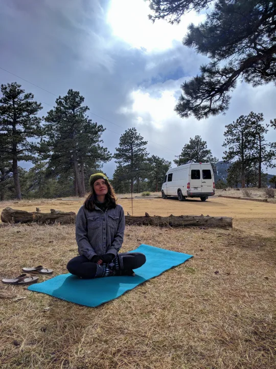 Woman practices yoga on a mat beside her RV rental, amidst pine trees under a cloudy sky.. Mercedes-Benz Sprinter 2005
