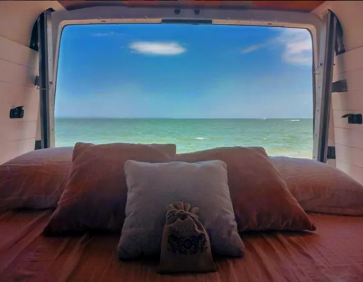 Cozy RV rental bed with pillows faces the ocean, offering tranquil views. Relax with your Blissle pouch.. Mercedes-Benz Sprinter 2005