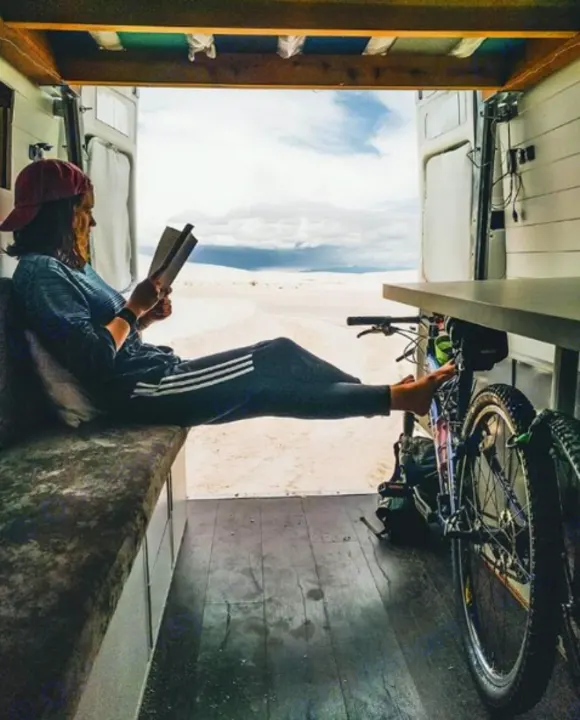 A woman reads in an RV rental, feet on her bike, gazing out at the vast desert. Perfect van life adventure!. Mercedes-Benz Sprinter 2005