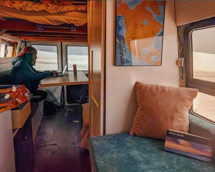 Experience remote work in a spacious RV rental. Person on laptop by window with White Sands view. Van interior with map, comfy seat.. Mercedes-Benz Sprinter 2005