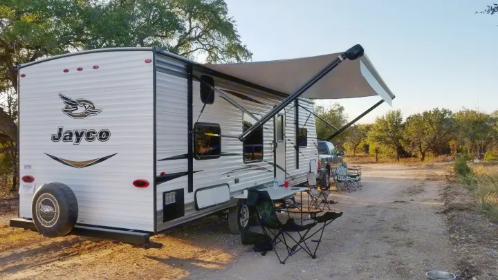 Relaxing at a scenic campsite with this RV rental. Jayco travel trailer with extended awning, chairs, and table.. Jayco Jay Flight 2018
