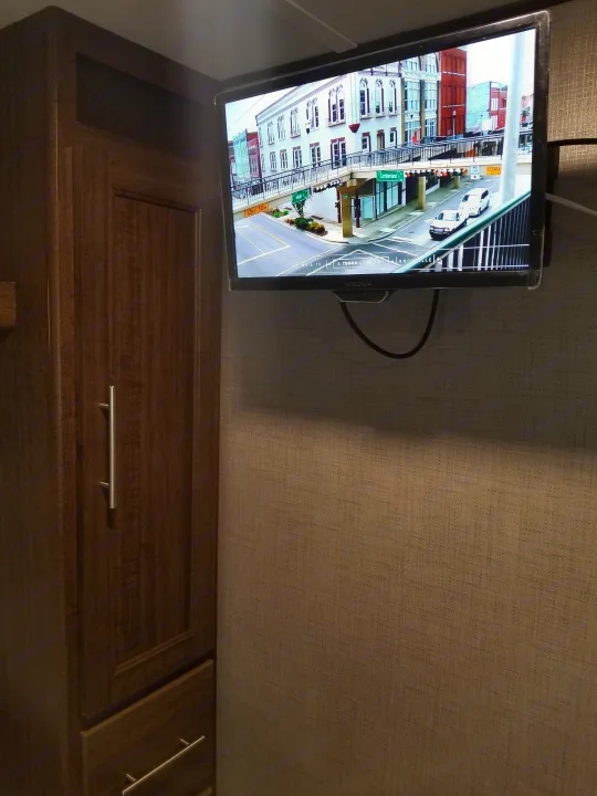 This RV rental interior features a TV displaying a street scene, positioned next to a tall wooden storage cabinet, ideal for compact living.. Crossroads RV Zinger Lite 2019