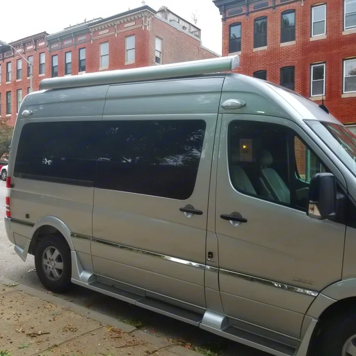 A silver Mercedes Sprinter camper van, ideal for rv rental, parked on a city street beside brick buildings.. Roadtrek Ssagile 2014