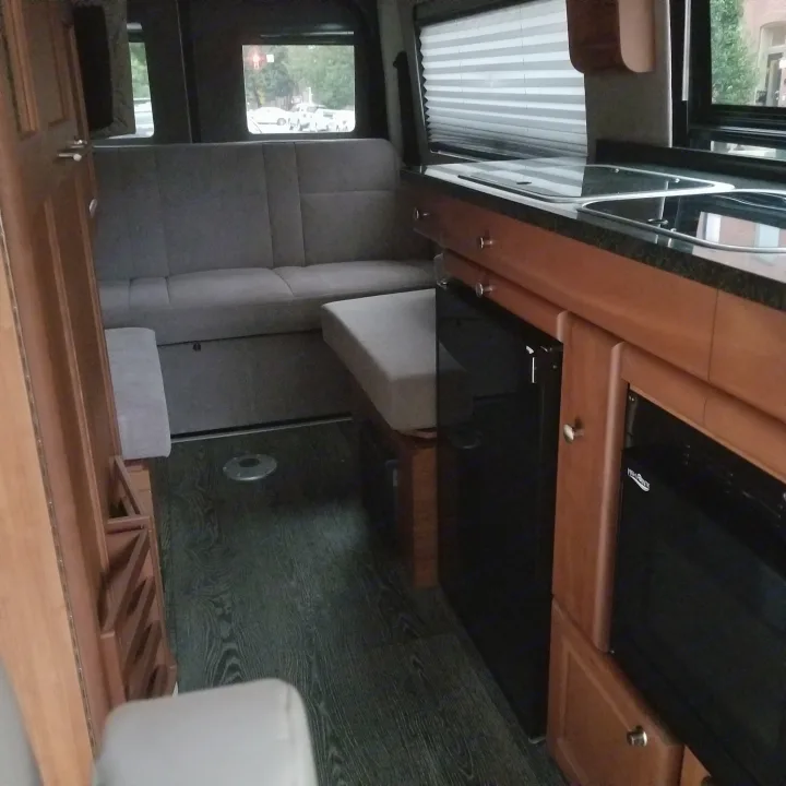 Explore this compact RV rental interior, featuring a cozy seating area, kitchen with appliances, and durable flooring.. Roadtrek Ssagile 2014