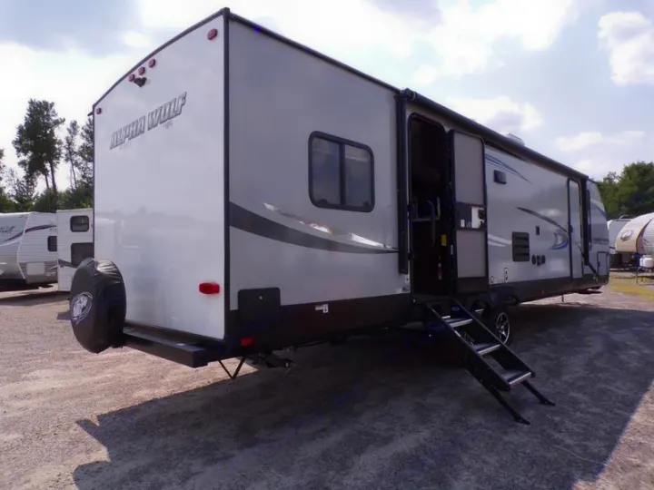Grey Alpha Wolf travel trailer, an ideal RV rental, parked outdoors with steps and a rear spare tire.. Forest River Alpha Wolf 2020