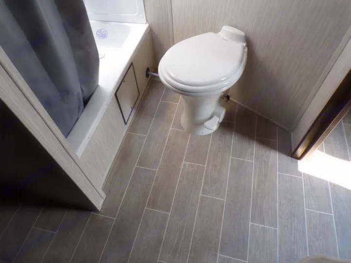 Inside an RV rental: a compact bathroom features a white toilet, shower with grey curtain, and wood-look tiled floor.. Forest River Alpha Wolf 2020