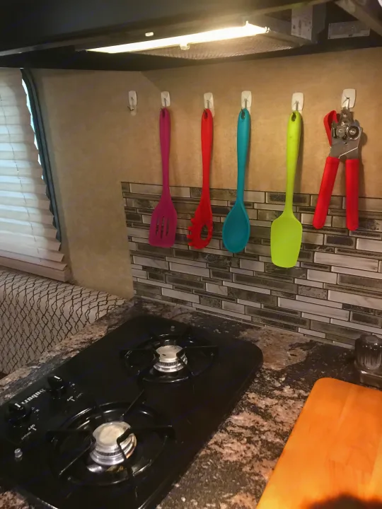 Compact RV rental kitchen with a two-burner stove, granite-look counter, tiled backsplash, and colorful hanging silicone utensils.. Starcraft Launch 2017