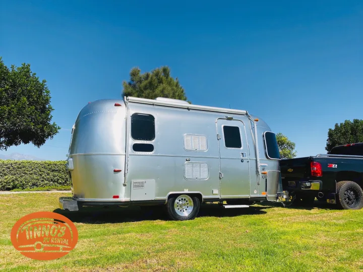 Shiny Airstream RV rental hitched to a black pickup truck on a green lawn under a clear blue sky. Explore now!. Airstream 19 Bambi International 2012