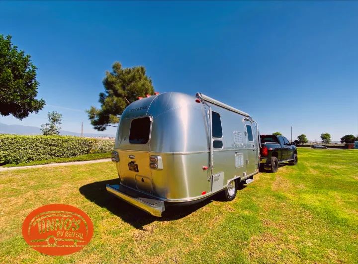Shiny Airstream RV rental trailer parked with a pickup truck on green grass under a clear sky.. Airstream 19 Bambi International 2012